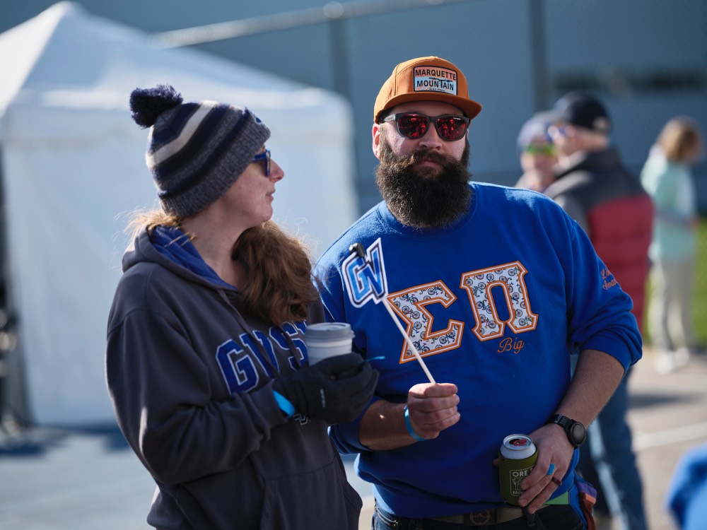 Man with sunglasses looking at camera, woman next to him wear hat looking off to the side